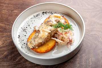 A gourmet dish featuring two golden cornbread slices topped with creamy mushroom sauce, shredded chicken, and garnished with herbs. Presented on a minimalist white plate against a wooden background.