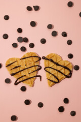 Vertical image of heart shaped cookies with melted chocolate and sprinkles scattered on a pink background. Valentine's Day concept