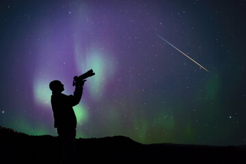 Man observing and photographing aurora borealis polar lights and Milky Way Stars from a dark countryside location. © astrosystem