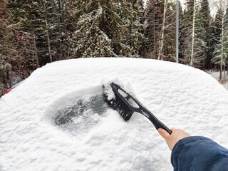 Hand brushes snow off a car on a cold winter day while preparing for travel