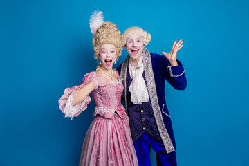 Elegant couple in vintage attire posing against a vibrant blue background, showcasing historical fashion with a modern twist.