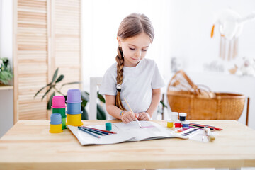 a little girl draws drawings with multicolored paints or learns to draw in a bright children's room...