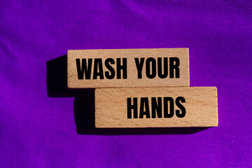 Obraz premium Wash your hands message written on wooden blocks with purple background. Conceptual wash your hands symbol. Copy space.