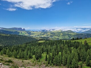 Idyllic mountain valley view, Italian Dolomites, rolling green hills and lush forests under a clear blue sky, mountains in the distant