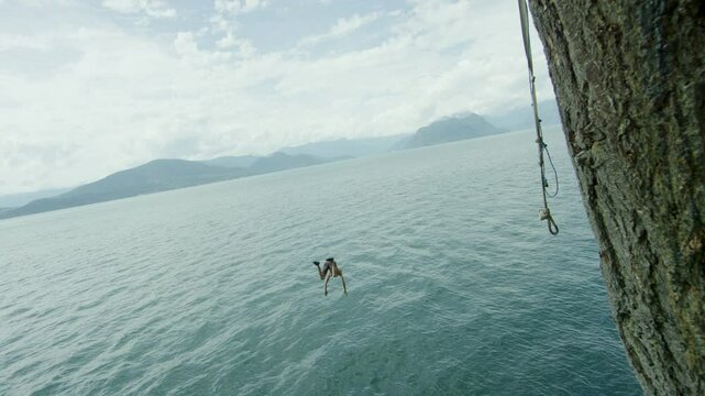 Man doing extreme backflip on tall rope swing over beautiful Canadian lake, slow motion