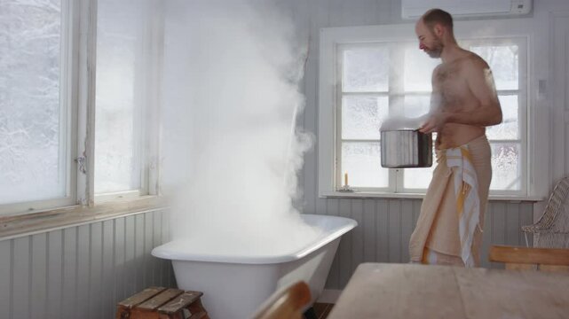 Bare chested man pours steaming hot water from pot into bath, wellness ritual