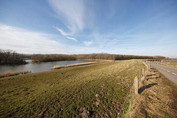 Fototapeta premium Vast grassland landscape by a serene lake with clear skies and scattered clouds on a bright sunny day