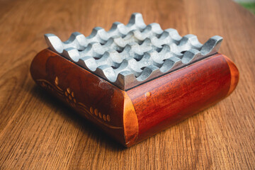 wooden ashtray with aluminum topping on wooden table. 2 harmonious objects