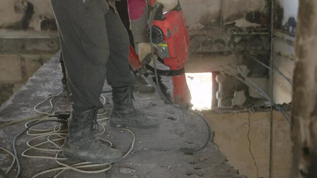 Construction workers use jackhammers to demolish damaged walls, ceilings in war-affected apartment. Dust-filled air, debris from concrete in renovation process. Laborers in protective gear working.