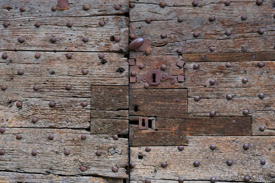 Background of two closed old unpainted and weathered and repaired wooden doors with keyholes and rusted door handles in Autoire Lot Occitanie in Southern France	