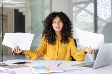 Portrait of confused and disappointed woman at workplace with papers and documents in hands....