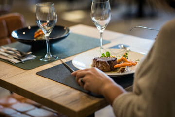 Une femme de dos mange un plat gastronomique à base de viande et de patate, elle tient dans ses...