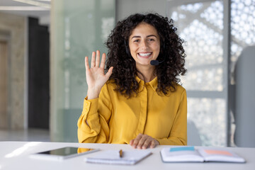 Webcam view, support worker smiling and looking into camera with headset, woman waving hello,...