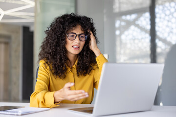 Upset and dissatisfied woman using laptop for video call. Office worker in glasses frustrated...
