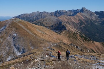 Scenery of autumn Tatras Mountains with two silhouettes of hiking persons. Czerwone Wierchy range from around Kasprowy Wierch Peak, Tatras Mountains, Poland.  