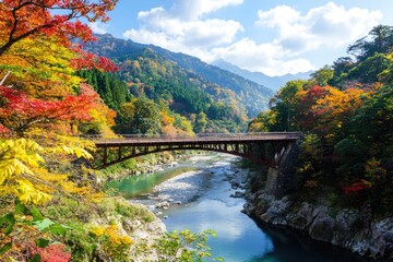 Fototapeta premium Ancient stone bridge arching over a lush river, surrounded by autumn foliage and rugged hills