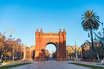 Obraz premium Sunrise view of the landmark Arc de Triomf in Barcelona in the morning with clear blue sky with golden warm light and no people in the Paseo de Lluís Companys. +