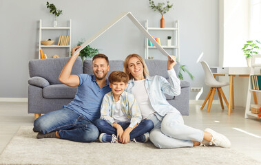 Portrait of happy young smiling family with their little child boy sitting on floor at home making...
