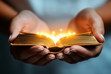 A person is holding an open book with a glowing light shining through it