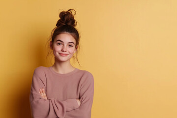 Obraz premium Portrait of positive girl with bun hairstyle, wearing casual sweater standing against yellow background