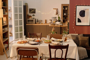 High angle shot of table with cotton tablecloth and served with healthy homemade food in cozy living room, contemporary decorated with golden lights kitchen in blurred background