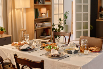 Medium close up of table covered with cotton tablecloth and served with Greek salad, baked potatoes with olive oil mixed herbes de Provence and snacks