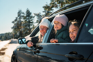 Mother and daughters enjoying a winter road trip, gazing out the car window at a stunning snowy...