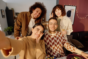 Brunette young adult woman smiling widely while taking selfie with her best friends during reunion party at home