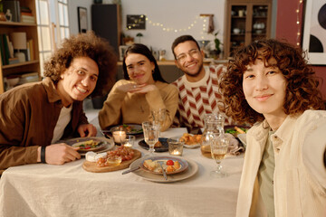 Medium close up of biracial friends sitting at served festive table looking at camera and posing