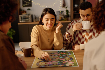 Fototapeta premium Medium close up of brunette woman enjoying her game turn while her boyfriend who sitting near her drinking tea