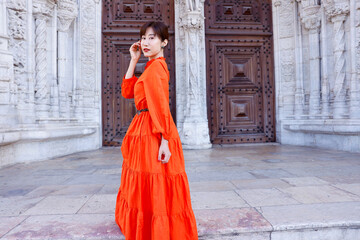 Naklejka premium A young beautiful asian woman stands in front of beautiful architecture in Lisbon, Portugal. She pushes her hair back out of her face in a spontaneous, candid, real moment. She smiles at the camera.