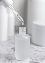 Drop falls from a pipette inside a glass dropper bottle against cosmetics in bathroom closeup