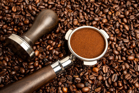 Portafilter and espresso tamper with coffee grinds on coffee beans 
