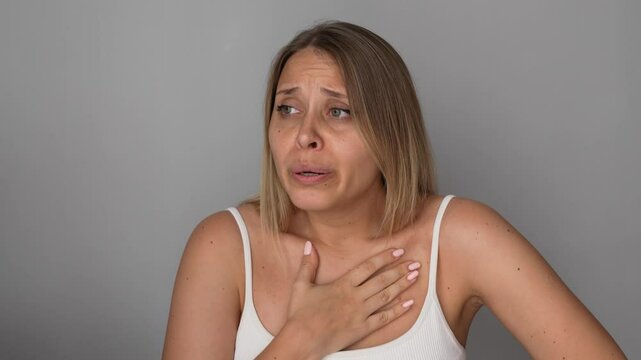Young blonde woman holding the chest with her hands suffering from panic attack on a grey background. Heartburn, pain, acid reflux, indigestion, osteochondrosis, neurological diseases. Chest tightness