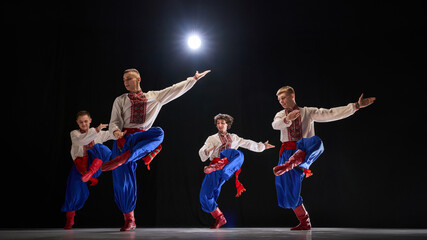 Male dancer leaping with arms stretched, traditional attire flowing, showcasing rhythmic motion and cultural storytelling against black studio background. Concept of traditions, folk style, people. Ad