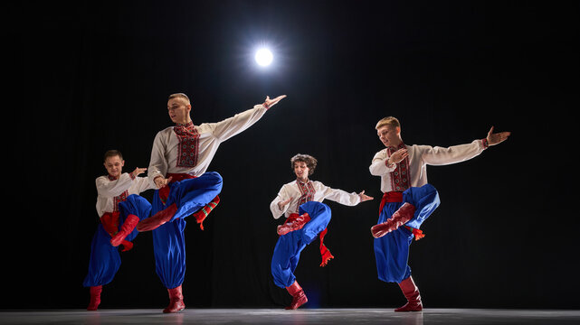 Male dancer leaping with arms stretched, traditional attire flowing, showcasing rhythmic motion and cultural storytelling against black studio background. Concept of traditions, folk style, people. Ad