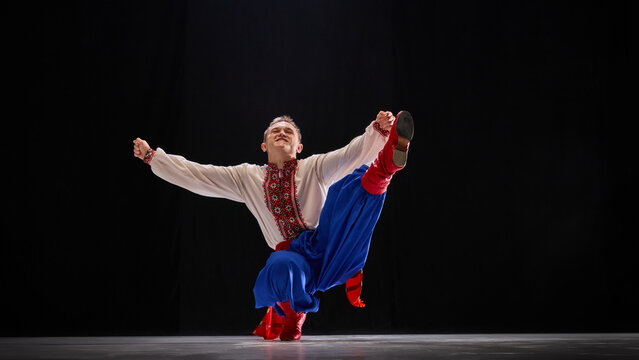 Male Ukrainian traditional dancer, dressed embroidered shirt and red boots, against black studio background. Freedom and culture. Concept of traditions, folk style, people, art and history. Ad