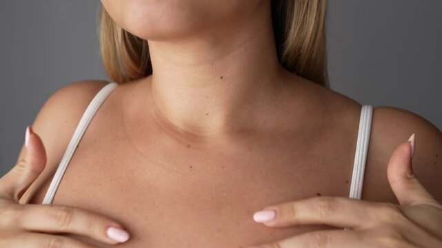 Young blonde woman showing lines on her chest and neck with her hands on a dark grey background. Wrinkles, age-related changes, rings of Venus, goosebumps. Creases on the skin. Close up