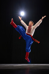 Performer leaping high, leg raised in powerful motion, arms outstretched, symbolizing freedom and culture in embroidered shirt and red boots. Concept of traditions, folk style, people, art and history
