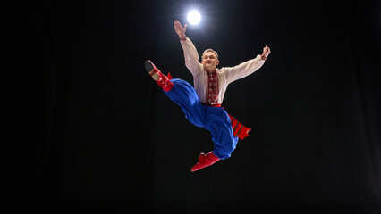 Graceful male dancer jumps with one leg forward, dynamic arms emphasizing energy and balance, symbolizing cultural expression and precision. Concept of traditions, folk style, art and history. Ad
