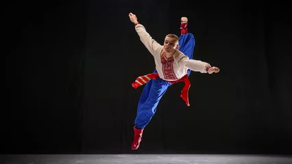 Fotobehang Male dancer in traditional Ukrainian attire, performing dance moves, showcasing strength and acrobatics of Hopak, against black studio background. Concept of traditions, folk style, art and history. © Lustre Art Group 