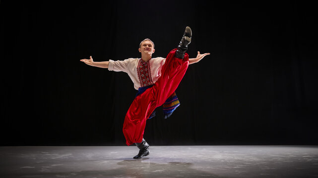 Dancer in traditional attire finishes with high kick, arms open in pride and confidence, highlighting boldness of Ukrainian cultural expression. Concept of traditions, folk style, art and history. Ad