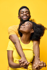 Obraz premium Happy young African couple embracing against a vibrant yellow background, showcasing love and joy in matching outfits, ideal for romantic and lifestyle themes