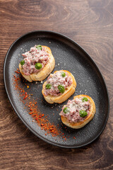 Delicious appetizer featuring three toasted bread slices topped with savory minced meat, cheese, and green peppers, garnished with a sprinkle of spices on a stylish black plate.