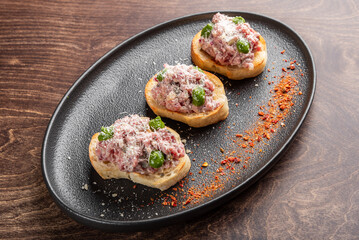 Delicious appetizer featuring three toasted bread slices topped with savory minced meat, cheese, and green peppers, garnished with a sprinkle of spices on a stylish black plate.