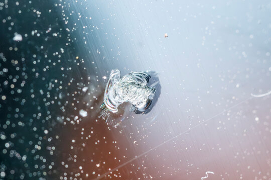 Close-up view of a windshield chip caused by gravel impact on a car during daytime