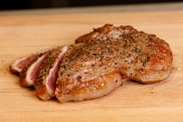 Sliced grilled steak resting on wooden cutting board garnished with pepper and herbs, perfect for dinner or special occasions