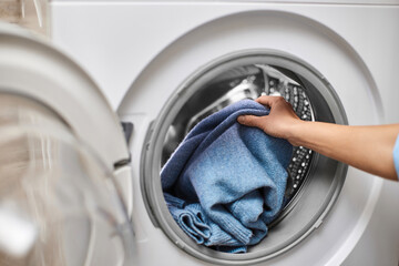 Woman putting blue wool clothes into the washing machine, close-up