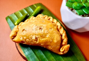 One piece of pastel sayur with green hot chilli pepper. Deep fried Indonesian traditional jajanan pasar dessert snacks isolated on horizontal orange brown terracota background with cactus decor.