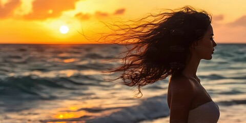 Fototapeta premium A model standing on a beach, their hair blowing in the sea breeze at sunset.